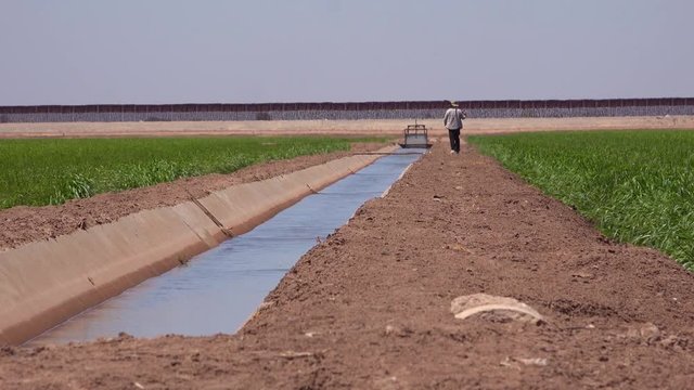 A farmer walks along the US Mexico border with the wall in the background.