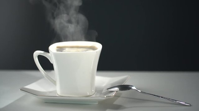A white cup of hot coffee with a stand  on a black background.