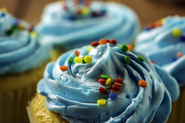 close up of yellow cupcake with blue frosting and rainbow sprinkles