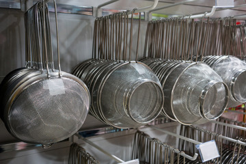 Many rows of silver metal colanders and strainers hanging on metal rack in store.