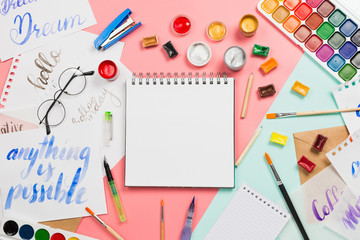 Beautiful flatlay arrangement with watercolors, brushes, glasses, brushpen, paints with notebook...