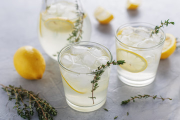 Homemade summer drink with lemon, thyme and ice in the glasses on the table. - obrazy, fototapety, plakaty
