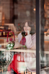 Beautiful girl looks through the window of a coffee house