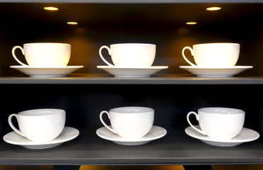 White cups and saucers stand in rows on shelves in a restaurant