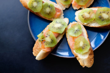 sandwiches with baguette, butter, salmon and kiwi lie on blue plate