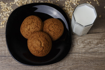 three oatmeal cookies lie on a black plate, beside scattered oat