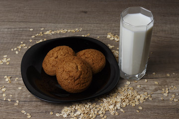 three oatmeal cookies lie on a black plate, beside scattered oat