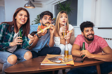 Group of young friends eating pizza and watching tv.Home party.Fast food concept.