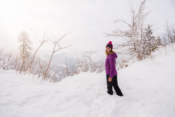 Young woman is standing in  deep snow dressed in colorful clothes and looking at the camera