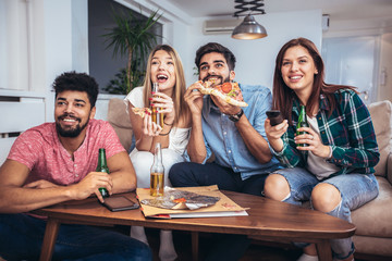 Group of young friends eating pizza and watching tv.Home party.Fast food concept.