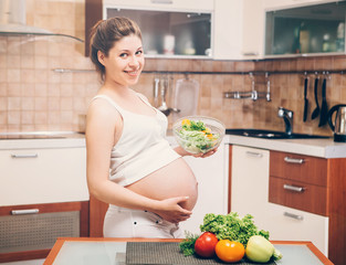 Healthy eating. Pregnant woman cooking healthy food while standing in the kitchen.