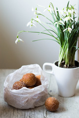mini donuts in a paper bag and snowdrops flowers on a white, woode table