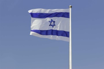 Israel flag flapping in the wind isolated against the blue sky. The flag is on a pole and flapping to the left. there are white clouds in the sky