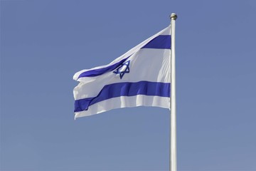 Israel flag flapping in the wind isolated against the blue sky. The flag is on a pole and flapping to the left. there are white clouds in the sky