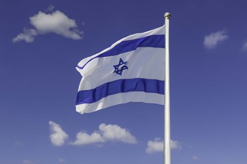 Israel flag flapping in the wind isolated against the blue sky. The flag is on a pole and flapping to the left. there are white clouds in the sky