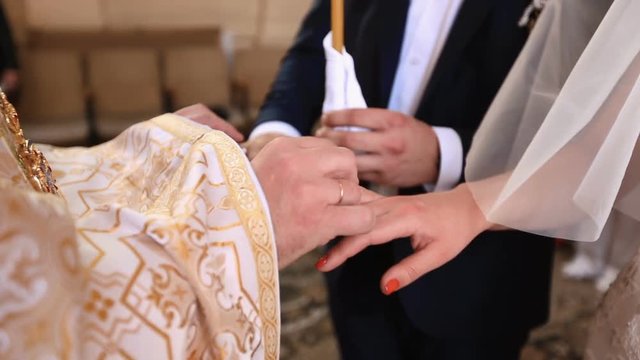 Close-up view of the priest hands putting the wedding rings on the hands of teh newlyweds. Wedding ceremony.