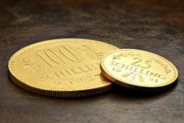 Austrian 25 and 100 Schilling gold coins on rustic wooden background