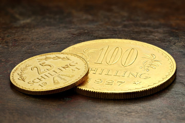 Austrian 25 and 100 Schilling gold coins on rustic wooden background