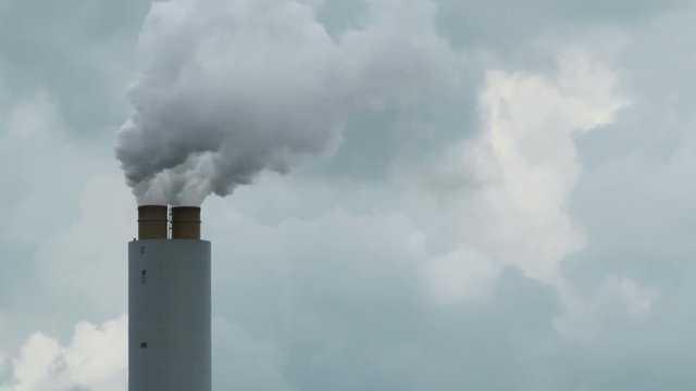 Close of shot of a smokestack emitting smoke and steam into a sky filled with clouds