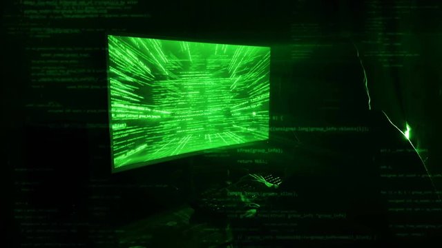 A man hacker in a hood in a dark room works with the program code