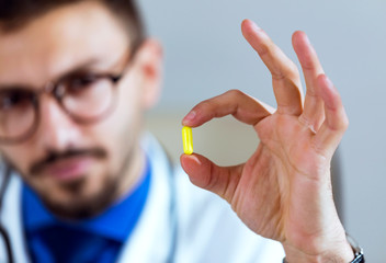 Confident male doctor looking and holding yellow pill in the office.