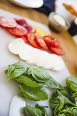 Slices of tomato, cheese, and basil lined up on a cutting board