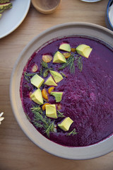 Close up of a bowl of purple beet soup topped with avocado chunks and dill