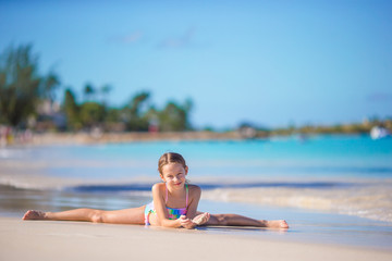 Adorable little girl lying in shallow water on white beach