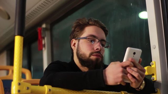 Man sitting in the bus and using white smartphone he look at the sreen and he finger taping on touchscreen. Internet swinning