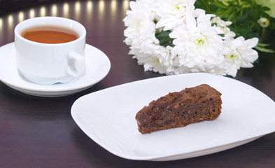 brownie cake on a white plate decorated with chrysanthemum flowers prepared for tea with a mug of tea