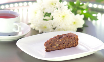 brownie cake on a white plate decorated with chrysanthemum flowers prepared for tea with a mug of tea