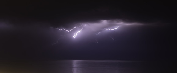 lightning bolts reflection over the sea. taken during a thunderstorm over the ocean with clouds in the background