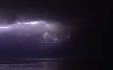 lightning bolts reflection over the sea. taken during a thunderstorm over the ocean with clouds in...