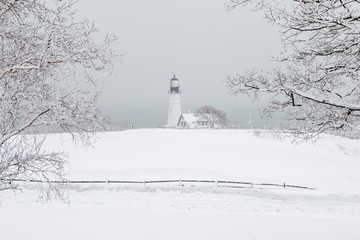 A dreamy snow covered landscape in Maine with a lighthouse in the distance. 