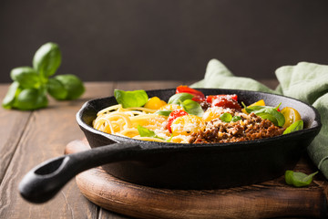 Delicious spaghetti Bolognaise or Bolognese with savory minced beef and cherry tomatoes garnished with parmesan cheese and basil in cost iron pan. Healthy italian food. Copy space.