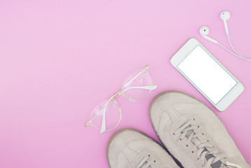 Sneakers, phone, glasses and headphones on the pink pastel background. Flat lay composition on a bright background with a place for text