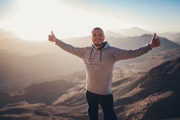Happy man stands against background of sunrise in Sinai mountains.