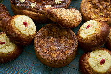 Traditional Russian Easter baked goods, kulichi, patties with cottage cheese, karavai and loaf cake with nuts on festive table background