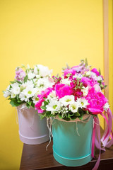 Bouquet of beautiful bright flowers in a cardboard round box of pastel color on a yellow background.