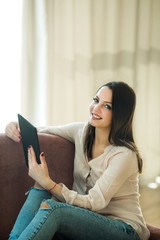 beautiful young girl with dark hair sitting on sofa with tablet