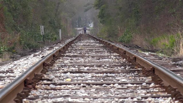 An old black man walks in the distance on lonely railroad tracks.