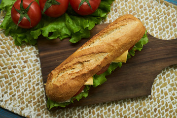 Fresh submarine sandwiches with chicken breast cheese, tomatoes, lettuce, cucumbers and onions on dark wooden cutting board, rustic background