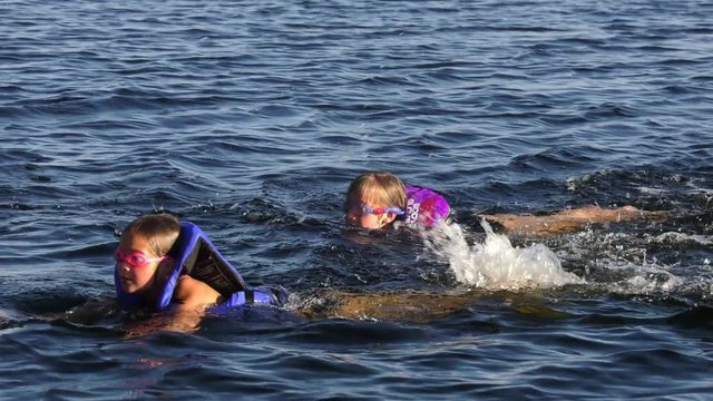 young girls swimming in lake together with life jackets and goggles