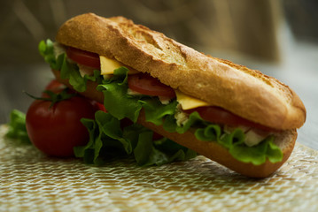 Baguette sandwich with turkey breast, cheese, lettuce, tomatoes and onion on a cutting board. Long subway sandwich on a rustic background, close-up