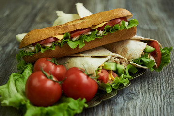 Shaurma chicken roll in a pita with fresh vegetables and long subway sandwich with tomatoes, cucumber, latitude, cheese and chicken breast fillet meat on wooden table, close-up