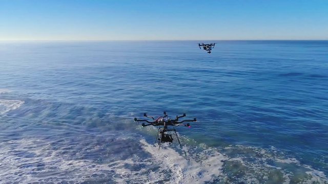 Aerial orbit view from a drone filming two drones at the beach on a sunny day.