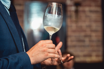 man in a blue suit holds glass of white wine