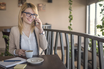 Business woman talking on smartphone and taking a notes, in a coffee shop, restaurant