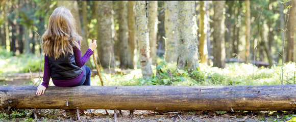 Young girl with long hair sitting on a tree log in autumn forest. Hiker woman resting.