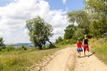 Fototapeta premium A boy and a girl children walk on a dirt road on a sunny summer day. Kids holding hands together while enjoying ativity outdoors.